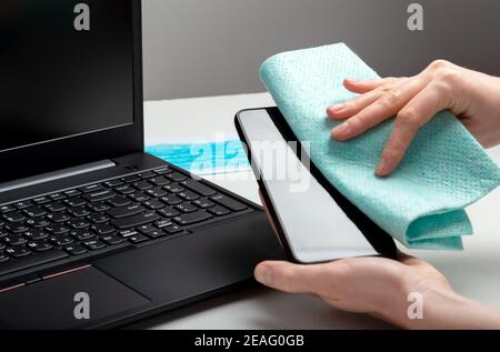 Donna pulizia smartphomeon spazio di lavoro. Disinfezione phomeand tastiera laptop con disinfettante alcolico. Donna pulizia delle superfici della scrivania dell'ufficio. Nuovo Foto Stock