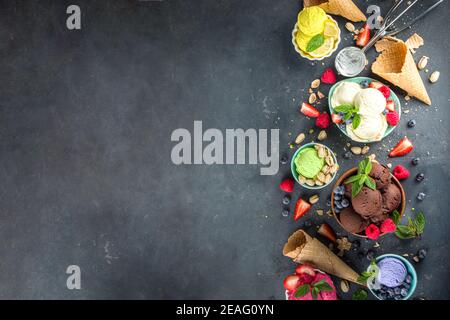 Varie palline colorate di gelato in diverse ciotole, con coni di cialde di gelato e ingredienti di sapore - pistacchio noci, bacche, limone, cioccolatini, Foto Stock