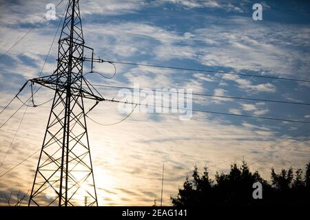 Un polo di potenza costruito sulla base di un traliccio contro il cielo e le nuvole al tramonto. Foto Stock