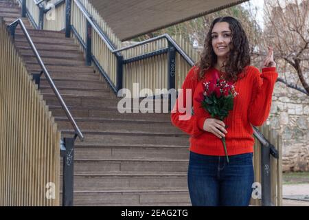 Bella donna che tiene un bouquet di fiori con le dita incrociate in un parco Foto Stock
