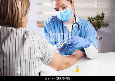 Giovane donna medico vaccinare la paziente anziana in UK GP's Office, virus terapia di malattia e trattamento, rimedio e cura per le infezioni o stagionale influenza Foto Stock