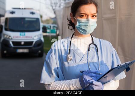 Preoccupato & ansioso medico di SME di NHS del Regno Unito, tenendo il modulo di rapporto del paziente piegatrice, in piedi davanti all'auto ambulanza, stanco e esausto dal lavoro turni lunghi,o Foto Stock