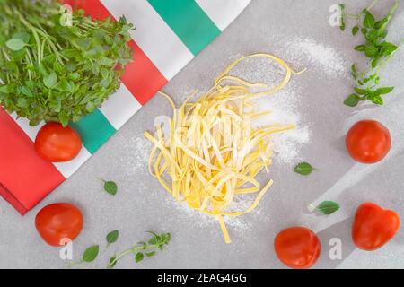 Tavolo da cucina, vista dall'alto, pasta fatta in casa, pomodori maturi e basilico verde, tovagliolo con tricolore italiano Foto Stock