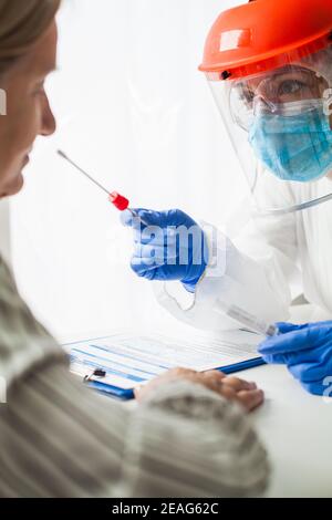 COVID-19 rt-PCR procedura di test, medico in DPI indossando tuta di nocciolo, viso schermo e maschera, paziente femmina con swabbing, campione nasofaringeo nasale coll Foto Stock