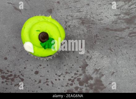 Vista dall'alto di un cupcake verde decorato con glassy glassed con accenti sfalsati su uno sfondo grigio. Foto Stock