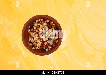 Vista dall'alto di una piccola ciotola in argilla con una porzione di aglio e peperoncino con un offset di stagionatura su uno sfondo dipinto di giallo. Foto Stock