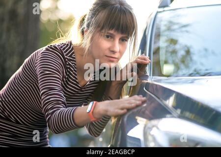 Giovane cliente donna che esamina attentamente una nuova auto presso il negozio all'aperto del concessionario prima di acquistarla. Foto Stock