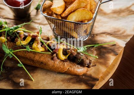 Barbecue hot dog alla griglia e birra con senape gialla e ketchup su sfondo di legno. Sandwich hot dog con patatine fritte e salse. Foto Stock