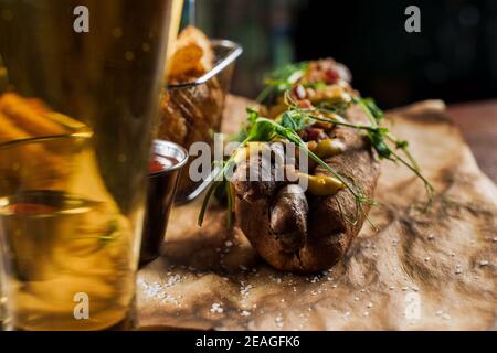 Barbecue hot dog alla griglia e birra con senape gialla e ketchup su sfondo di legno. Sandwich hot dog con patatine fritte e salse. Foto Stock