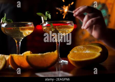 Festeggiamo il nuovo anno 2022 con fuochi d'artificio sparklers e cocktail. Menta con fetta di arancia in un bicchiere da cocktail pieno di cocktail alcolico Foto Stock