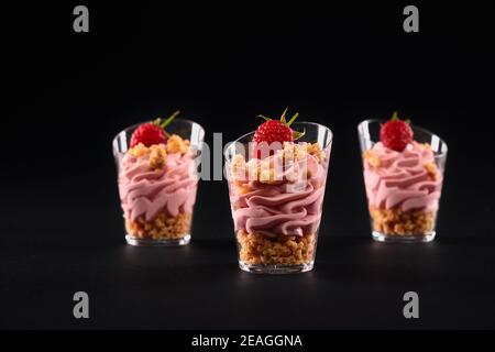 Vista in primo piano del dolce fresco fatto in casa in tre piccoli bicchieri di fila. Gustoso parfait con muesli, decorato con lamponi e whi rosa Foto Stock