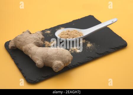 Primo piano di una tavola in cui è presente un frammento di una radice di zenzero accanto ad un cucchiaino da tè con zenzero in polvere Foto Stock