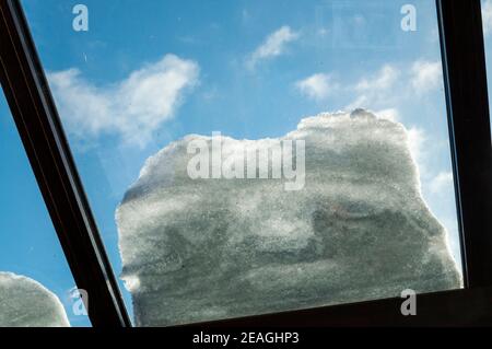 Neve sul tetto di vetro di una serra isolata con doppi vetri, vista dall'interno. Contro un cielo blu. Foto Stock