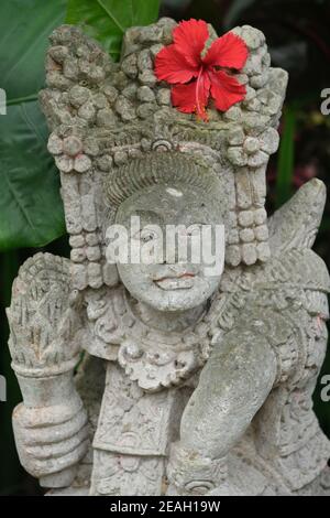Indonesia Bali - Ubud statua in pietra balinese fatta a mano con rosso Fiore di Hibiscus Foto Stock