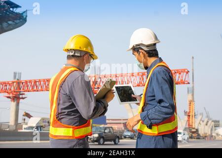 Due tablet per lavoratori ingegneri che lavorano sulla costruzione di strade in cantiere, un uomo asiatico costruttore di architettura costruire geometra professionista Foto Stock