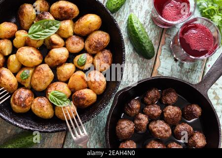 Cucina scandinava. Patate fritte, polpette di carne e beva di mirtillo serviti con verdure ed erbe sulla vista panoramica rustica del tavolo blu Foto Stock