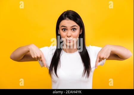 Foto di sorpresa eccitato carino caucasica ragazza puntando le dita verso il basso, in piedi su isolato sfondo arancione, con volto scioccato e guarda la fotocamera Foto Stock