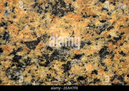 Granito giallo scuro con piccole inclusioni di colore nero, primo piano di una superficie piana lucida di pietra naturale. Sfondo, motivo, trama. Foto Stock