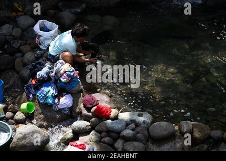 Dumaguete, le Filippine - 23 gennaio 2021: Donna che lava i vestiti nel fiume. Stile di vita rustico in Asia meridionale. I doveri della famiglia sulla donna. Lif. Resistente Foto Stock