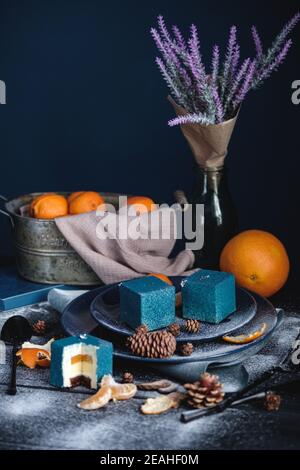Torta blu ripiena di arancio e mandarino a forma di cubo. Vicino su un tavolo nero sono ingredienti arance, mandarini, noci. Stile rustico. Foto Stock