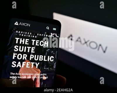 Persona che tiene smartphone con il sito web del produttore americano di armi Axon Enterprise Inc. Sullo schermo davanti al logo. Mettere a fuoco il centro del display del telefono. Foto Stock
