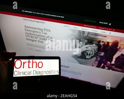 Persona che detiene smartphone con il logo della società americana Ortho Clinical Diagnostics sullo schermo di fronte al sito Web. Mettere a fuoco il display del telefono. Foto Stock