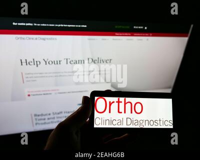 Persona che detiene il telefono cellulare con il logo della società americana Ortho Clinical Diagnostics sullo schermo di fronte alla pagina web aziendale. Mettere a fuoco il display del telefono. Foto Stock