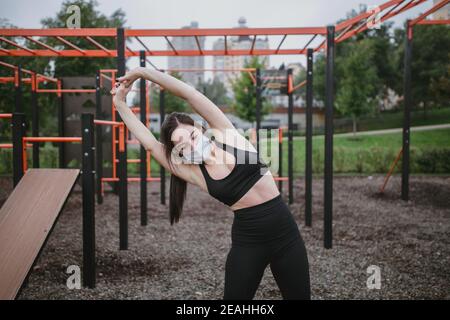 Una giovane donna fa gli sport sul campo da gioco che indossa una maschera coronavirus nuovo normale Foto Stock