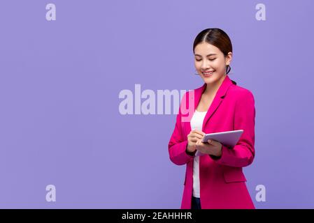 Bella donna asiatica intelligente in tuta da lavoro rosa utilizzando il digitale tablet isolato su sfondo viola Foto Stock