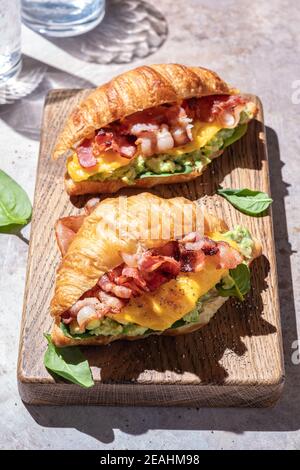 colazione a base di croissant con uova strapazzate, pancetta croccante e avocado al purè Foto Stock