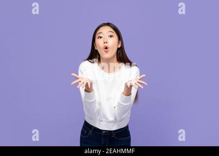 WOW sorpresa giovane ragazza asiatica con entrambe le mani aperte isolato su sfondo viola Foto Stock