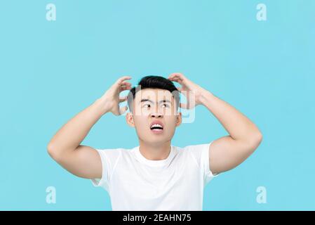 Arrabbiato uomo asiatico arrabbiato con le mani che stringono la testa isolato sfondo blu chiaro Foto Stock