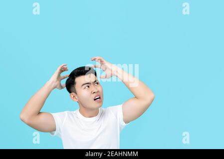 Arrabbiato uomo asiatico arrabbiato con le mani sulla testa isolato sfondo blu chiaro Foto Stock