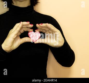 Una donna negli anni '50 indossando vestiti neri tiene un biscotto rosso a forma di cuore nelle sue mani su uno sfondo cremoso Foto Stock