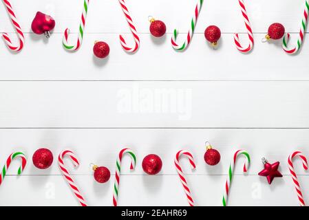 Vista dall'alto delle decorazioni natalizie e di oggetti come la caramella bastoni di canna e bulbi rossi disposti orizzontalmente in file su sfondo in legno bianco per f Foto Stock