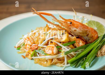 Primo piano di deliziosi piatti asiatici, gamberi freschi caldi Pad piatto di noodle tailandese guarnito con gamberi cipollotti cipollotti e lime Foto Stock