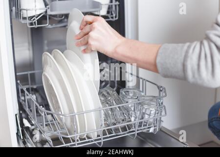 Lavori di casa: giovane donna di mettere i piatti in lavastoviglie. Foto Stock