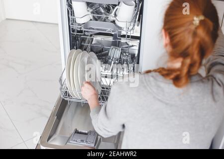 Lavori di casa: giovane donna di mettere i piatti in lavastoviglie Foto Stock