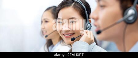 Sorridente bella donna asiatica telemarketing agente che lavora con il team in sfondo banner ufficio call center con spazio per la copia Foto Stock