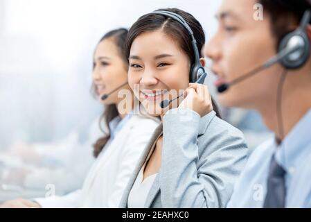 Sorridente bella donna asiatica agente telemarketing che lavora nel call center ufficio con il team Foto Stock