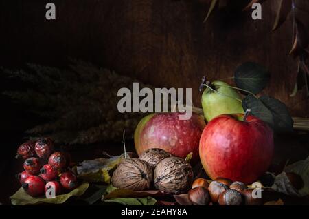 noci e frutta con fogliame in stile rustico al buio sfondo di legno Foto Stock