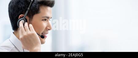 Sorridente bell'uomo asiatico che indossa le cuffie e lavora nel call center come operatore del servizio clienti su sfondo banner con copia spazio Foto Stock