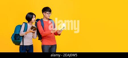 Giovani studenti asiatici maschi e femmine in colorati abiti casual guardando il libro isolato sfondo giallo banner con copia spazio per la co. eduction Foto Stock