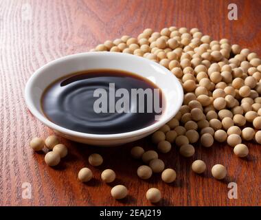 Salsa di soia in un piatto e fagioli di soia sparsi intorno Foto Stock