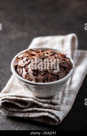 Cioccolato fondente grattugiato. Scaglie di cioccolato in ciotola su tovagliolo a scacchi. Foto Stock