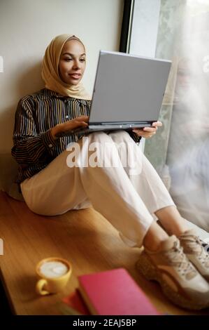 Ragazza araba seduta sul davanzale e usando il laptop Foto Stock