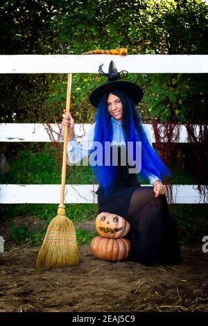 Una ragazza in costume da strega si siede su due zucche e tiene una scopa nelle mani Foto Stock