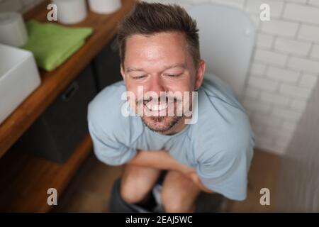 Uomo con sorriso soddisfatto si siede sulla toilette Foto Stock