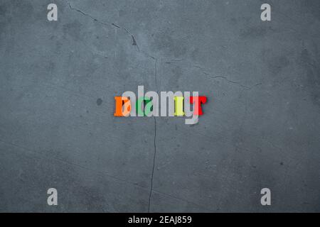 La parola multicolore Do IT è fatta di lettere di legno su uno sfondo grigio intonacato parete. Foto Stock