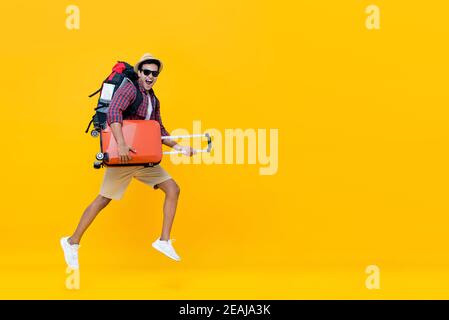 Sorridente eccitato bel turista indiano con zaino che tiene il bagaglio e saltando pronto per andare in viaggio isolato su giallo sfondo con copia s Foto Stock